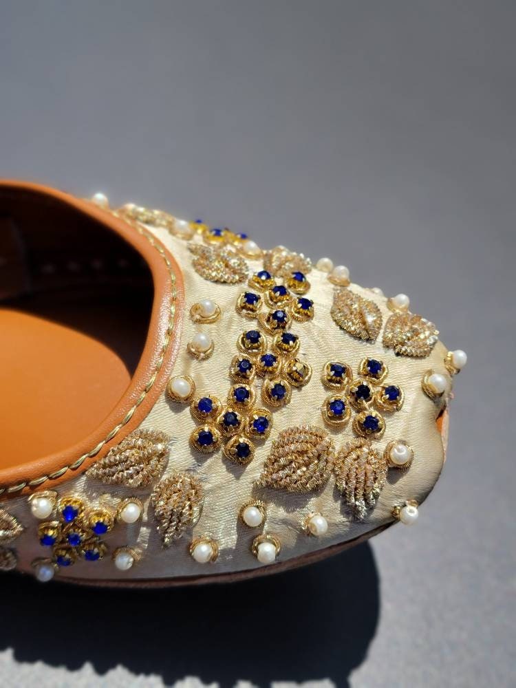 Gold base khussa with white pearls and blue diamonds and kora dabka work.